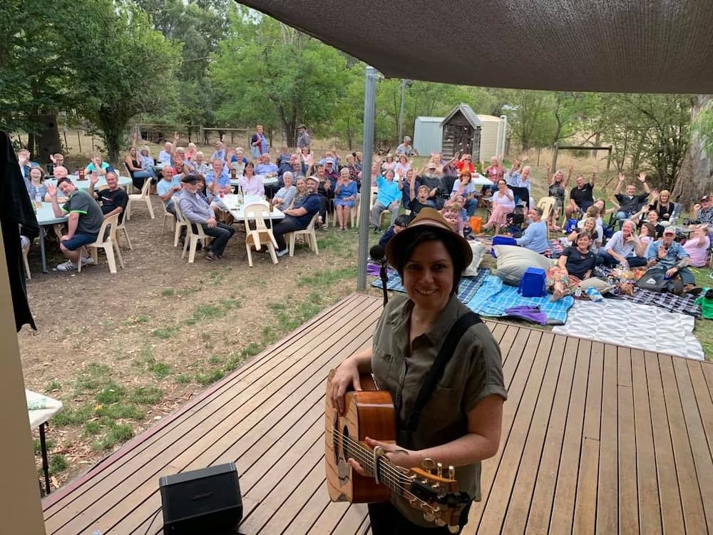 Jenny Biddle with a guitar in front of an audience outside the Fawcett Hall performing at the bushfire fundraiser in February 2020