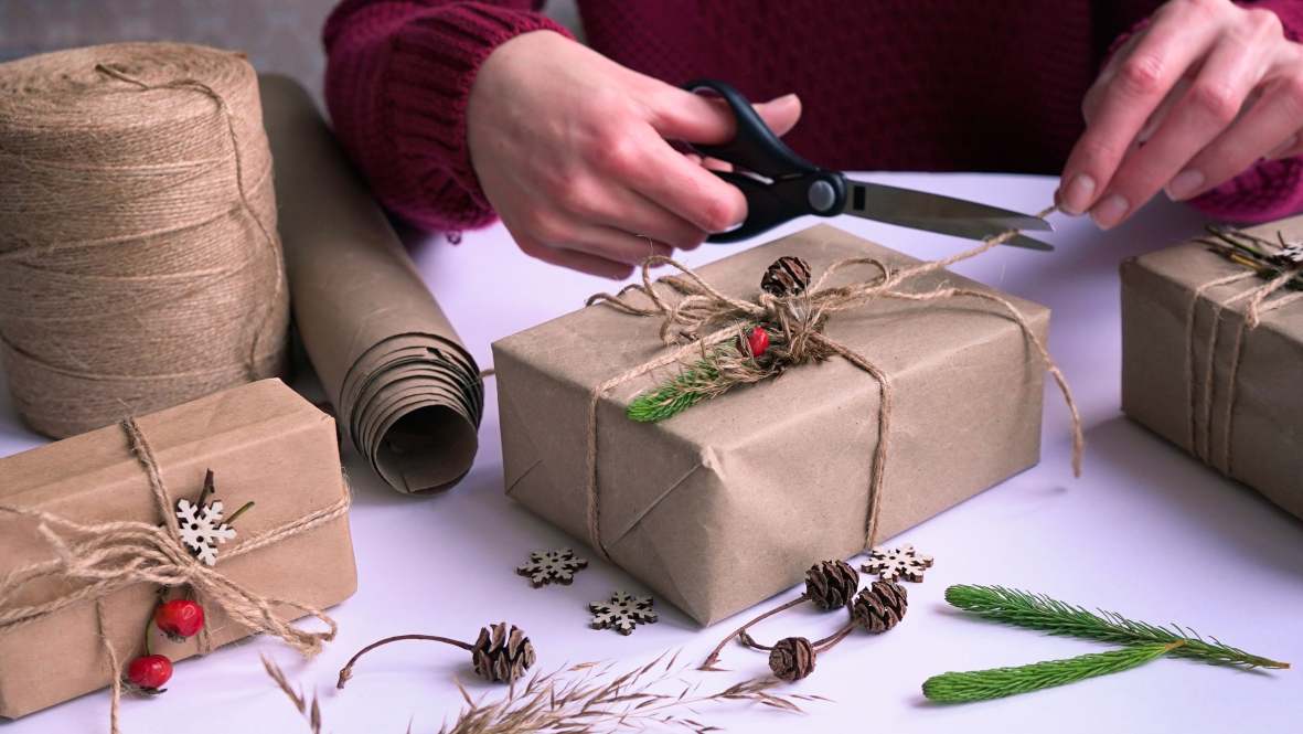 A person uses scissors to trim twine wrapped around a gift wrapped in brown paper.