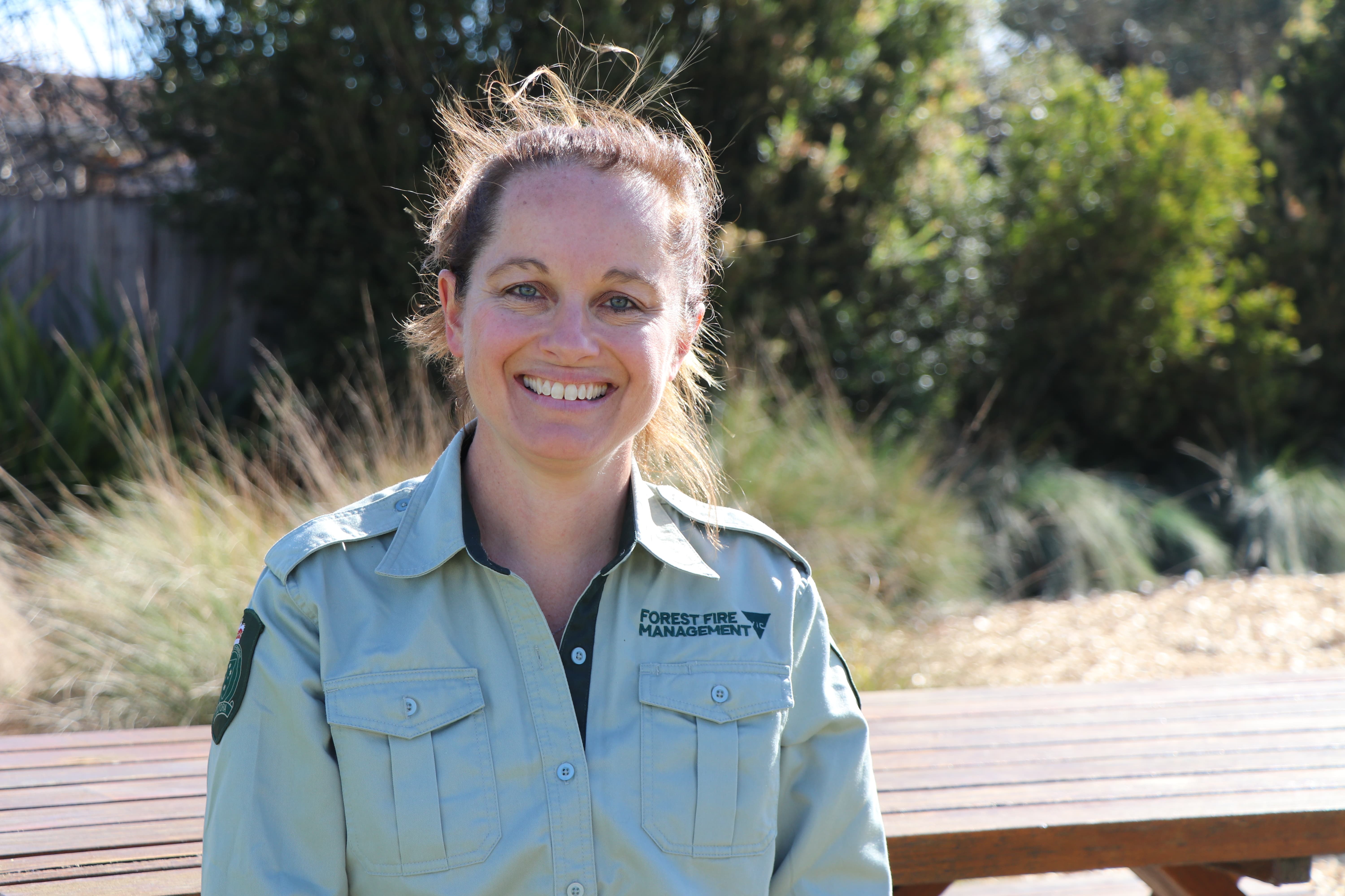 Kate Biles standing and smiling outdoors in her Forest Fire Management Victoria uniform.